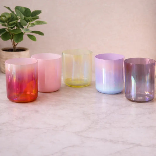 Set of colorful glass tumblers on a marble surface with a plant in the background