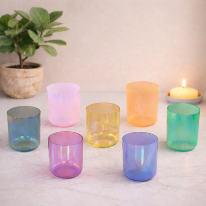 Set of colorful glass tumblers on a light surface with a plant and candle in the background.